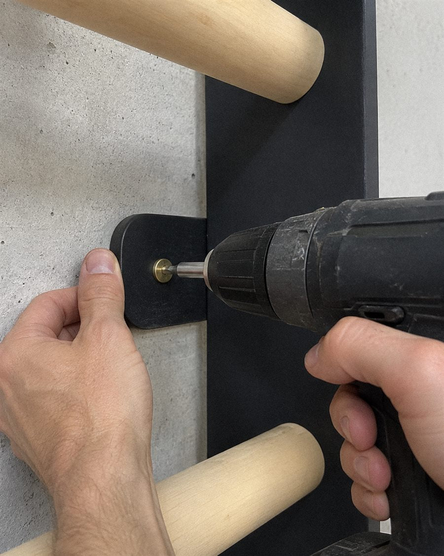 A close-up of a hand holding a drill, mounting an EZORA wall ladder bracket into a concrete wall