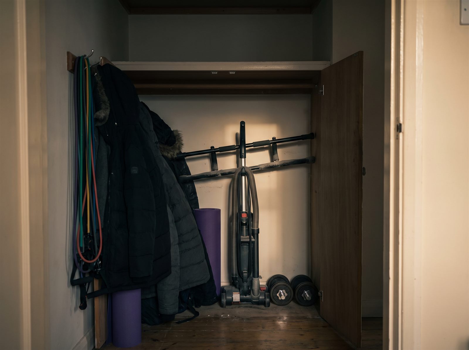 A cluttered closet with resistance bands, a rolled-up yoga mat, dumbbells and a doorway pull-up bar put away out of sight